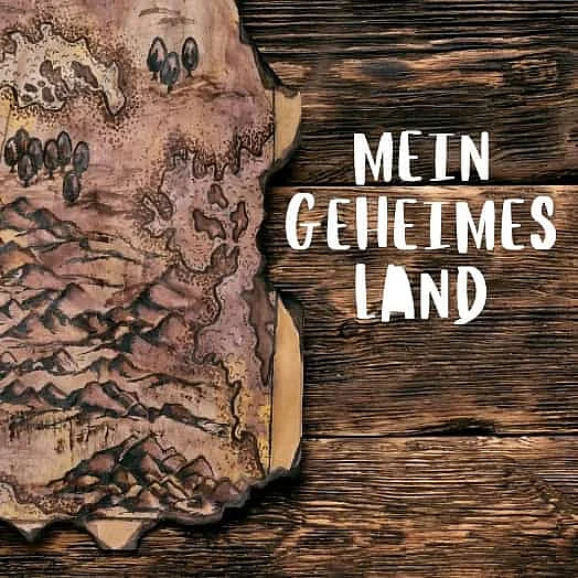 Die Grafik zeigt eine stilisierte, verbrannte Pergament- oder Schatzkarte auf einem dunklen Holzuntergrund mit dem deutschen Schriftzug Mein geheimes Land.