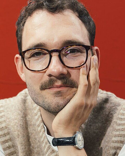 Porträt des Autors Lukas Rietzschel vor rotem Hintergrund